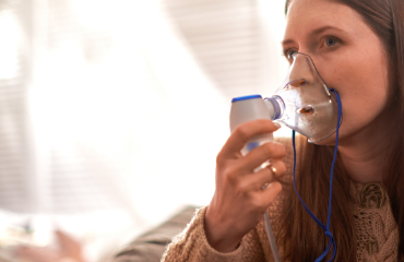Foto/Grafik Quelle: shutterstock.com [1255523245 Die Frau macht zu Hause einen Inhalationsnebelapparat. Halten Sie einen Maske-Neuling, der Dämpfe einatmet, sprühen Sie das Medikament in Ihre Lungenkranke. Selbstbehand
